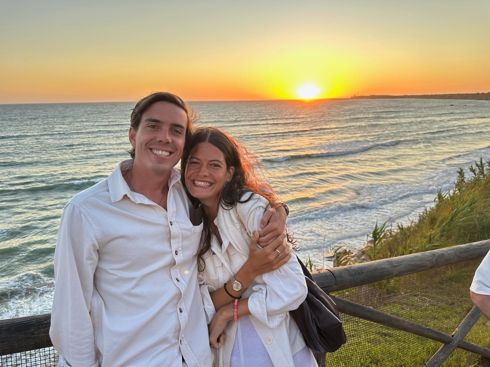 Pilar y Luis abrazados frente al mar al atardecer